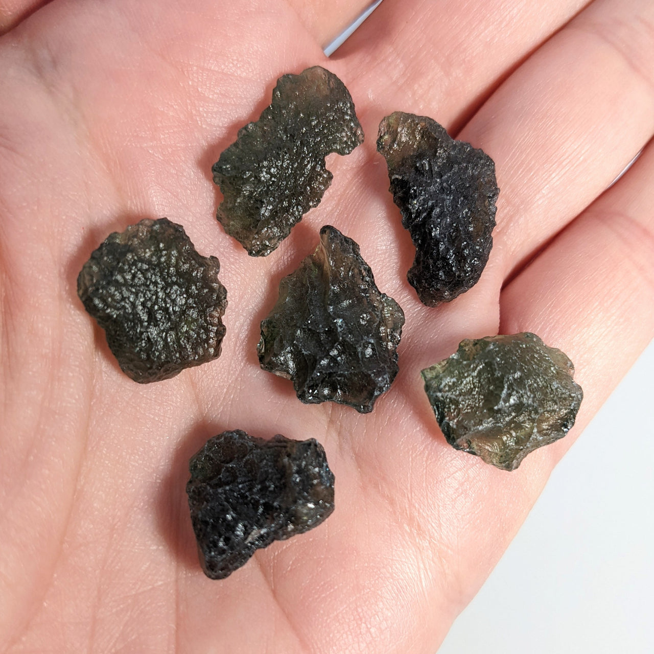 6 rough-cut moldavite crystals in the palm of the hand