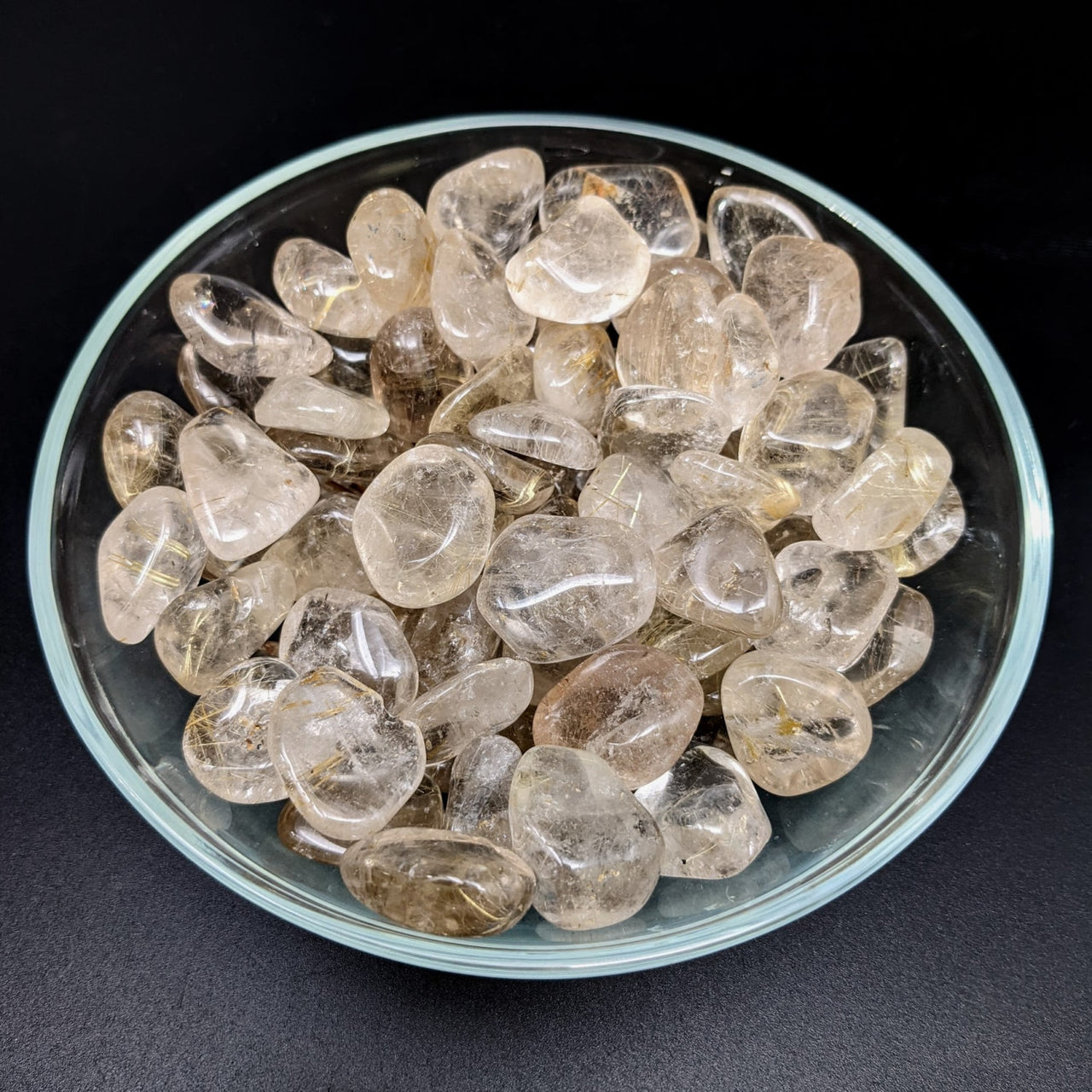 Clear quartz crystals in bowl alongside a rutilated quartz tumbled stone, product #LV1272