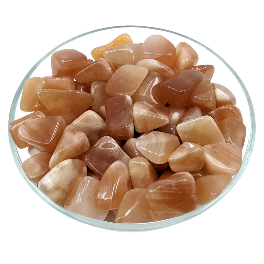 Polished peach moonstone crystals in a glass dish with Honey Calcite Tumbled Stone