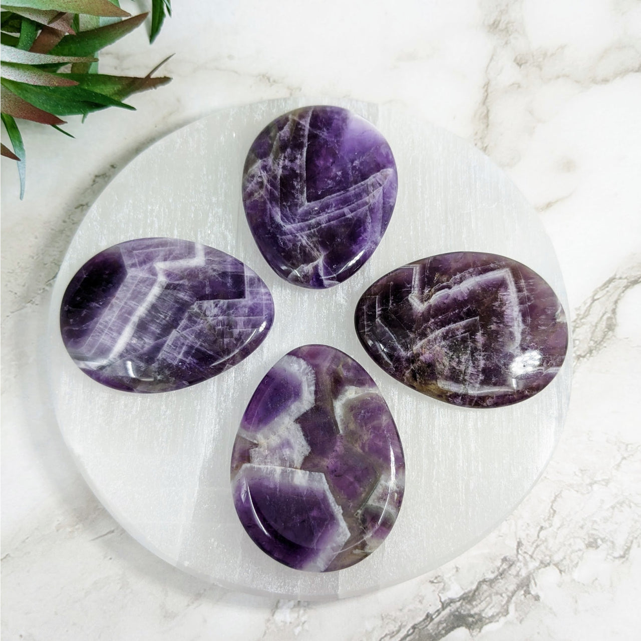 Amethyst 1.7’ Thumb Stone #LV4037 on marble plate with plant in background