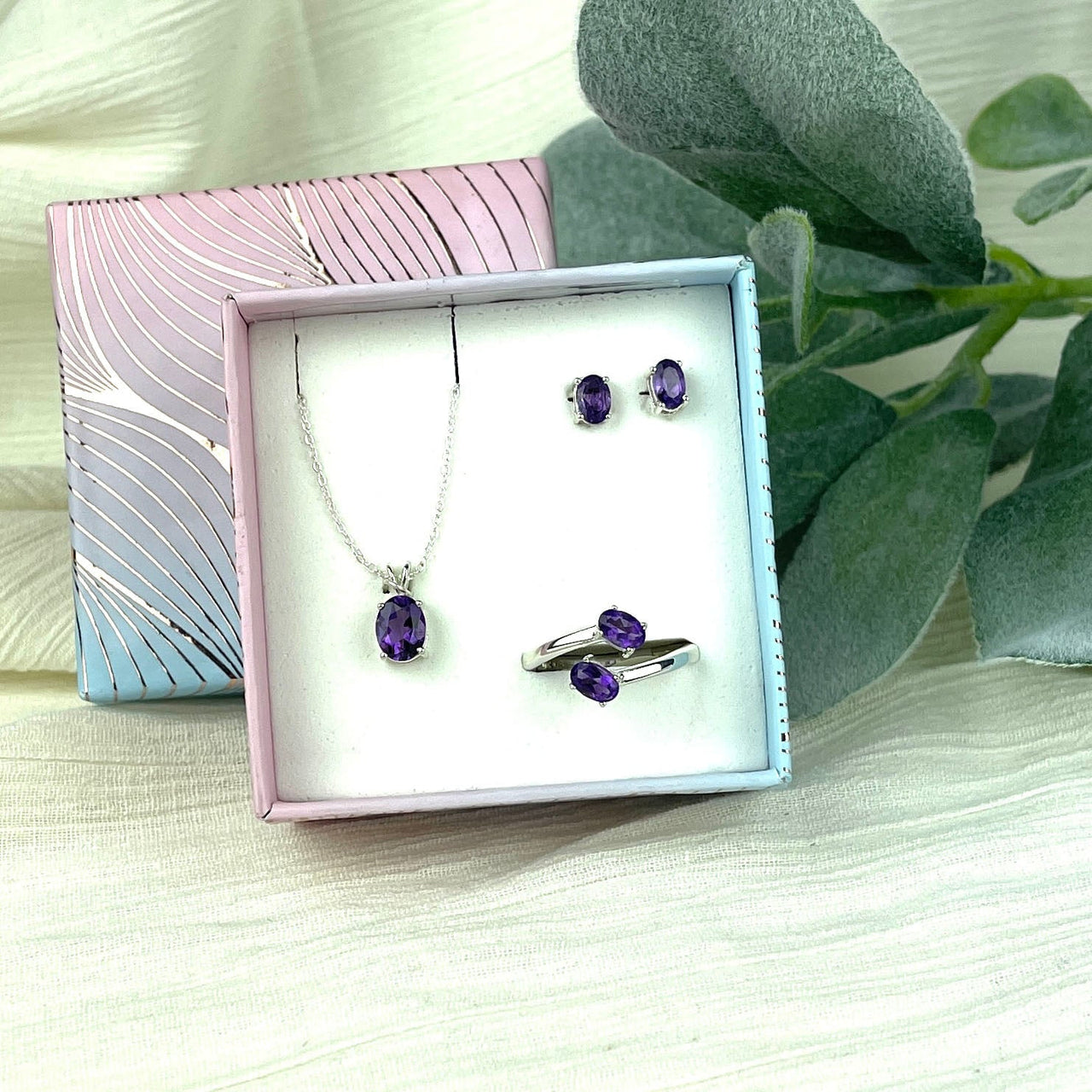 Amethyst faceted crystal jewelry set in sterling silver box with flower on a table