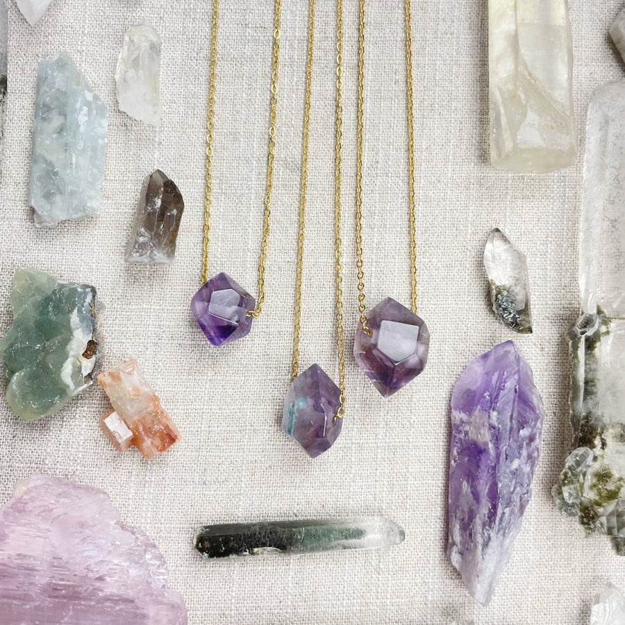 Three delicate gold chain necklaces with faceted amethyst pendants
