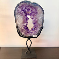 A stunning purple amethyst geode with crystalline interior and dark rim on a black metal stand for display