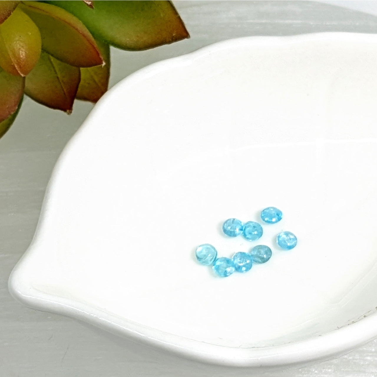 Light blue Aquamarine 2mm mini rondelle beads scattered on a white surface