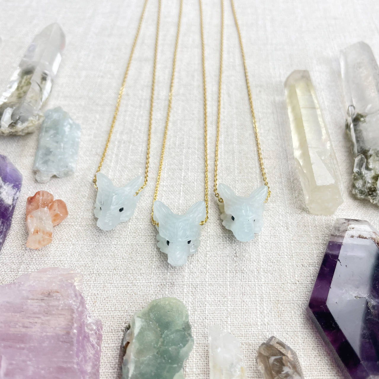 Three delicate gold chain necklaces with light blue jade fox pendants and black bead eyes