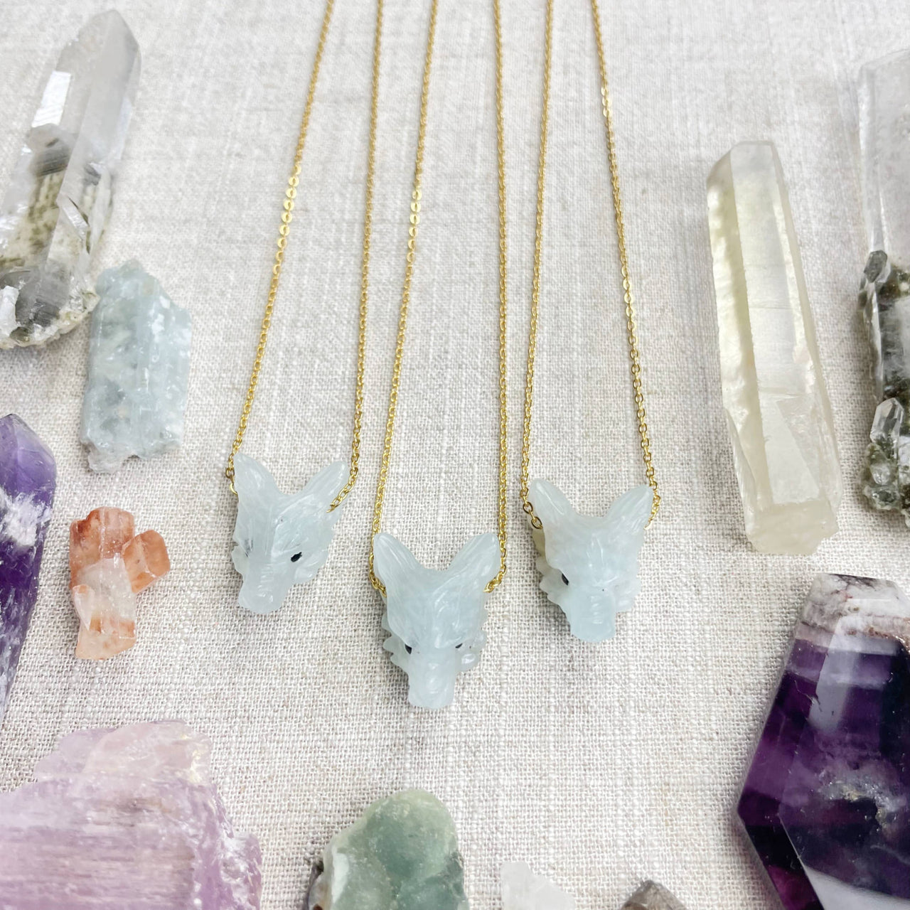 Three delicate gold chain necklaces with aquamarine carved wolf jade fox pendants