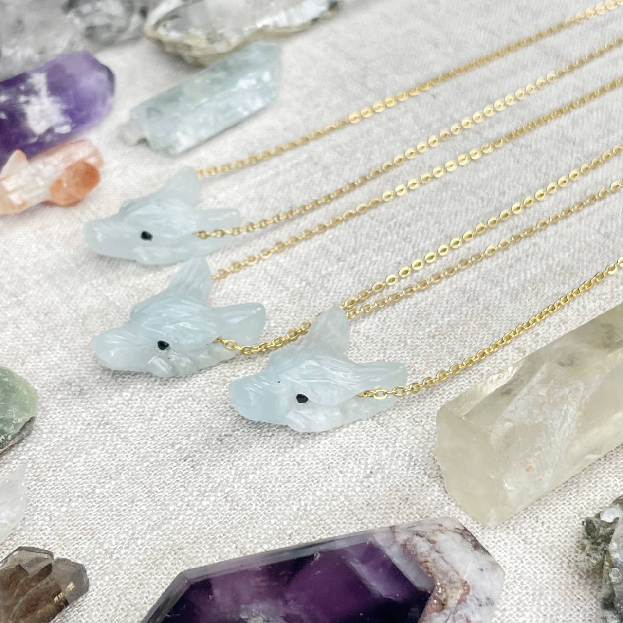 Three delicate gold chain necklaces with light blue jade wolf pendants