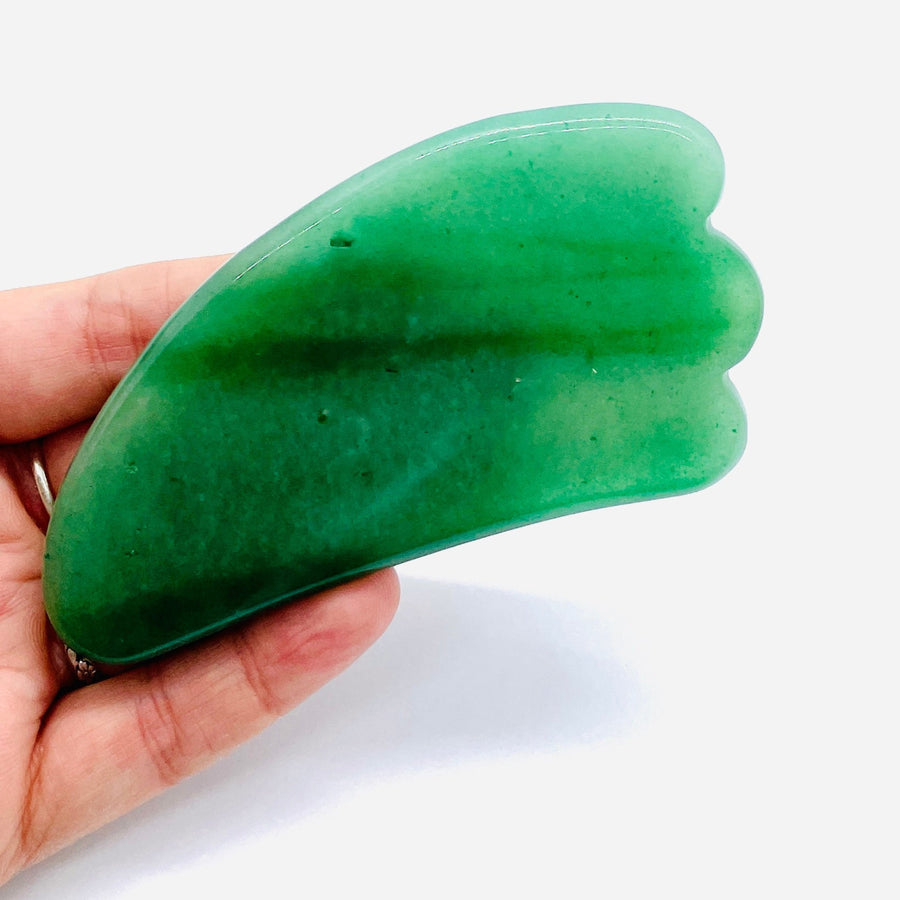 A hand holding a green jade stone gua sha massage tool from Assorted Crystal Gua Sha #K166