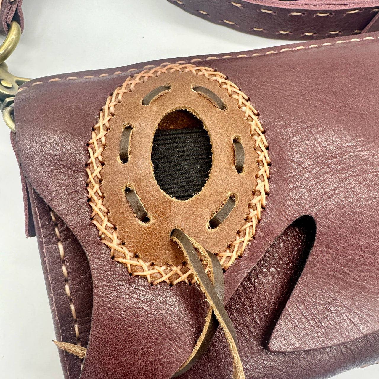 Maroon leather crossbody bag with hand-stitched oval cutout accent and woven details