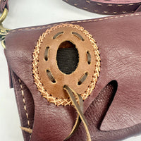 Maroon leather crossbody bag with hand-stitched oval cutout accent and woven details