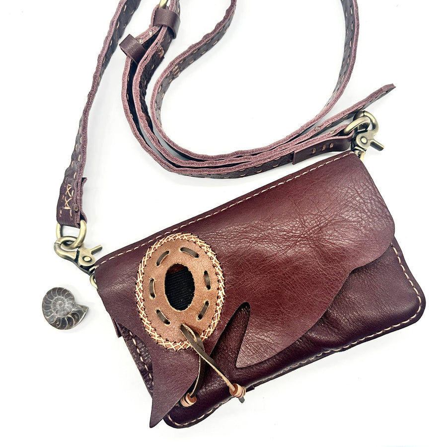 Maroon leather crossbody pouch with woven flap, oval cutout, and interchangeable stone