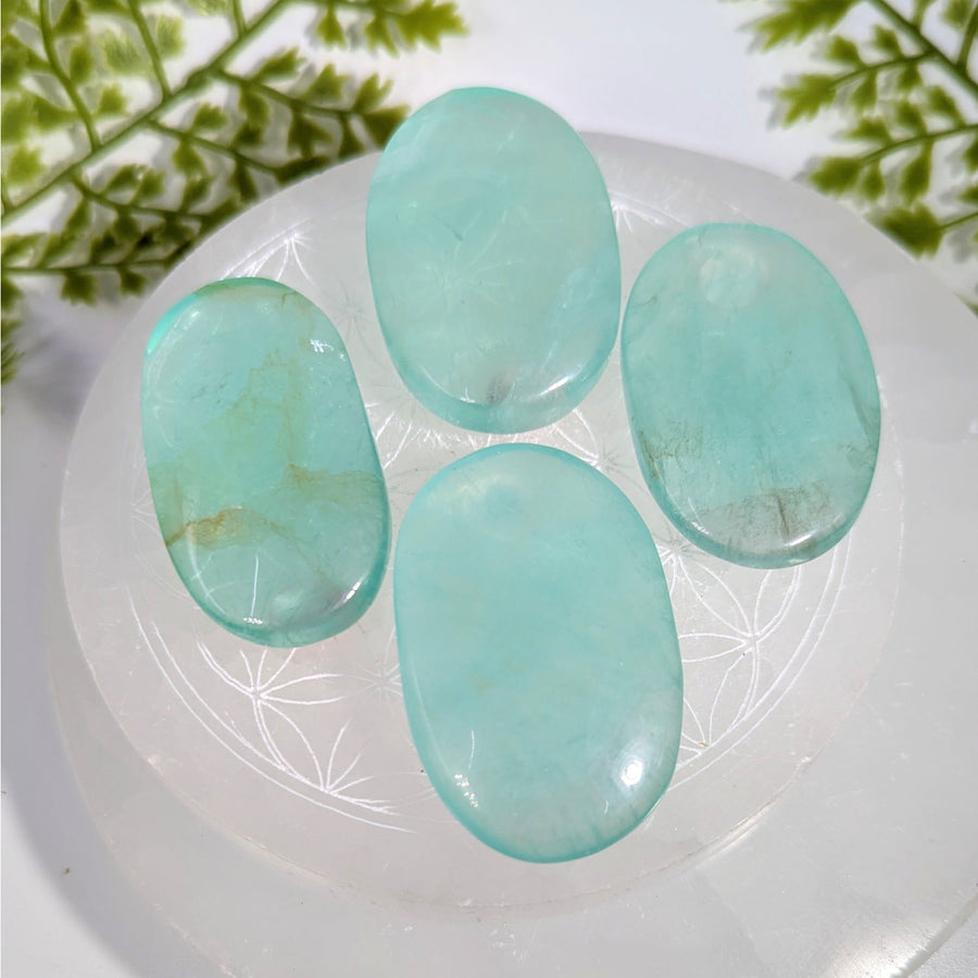 Four translucent light blue oval fluorite palm stones on white plate #BC0885