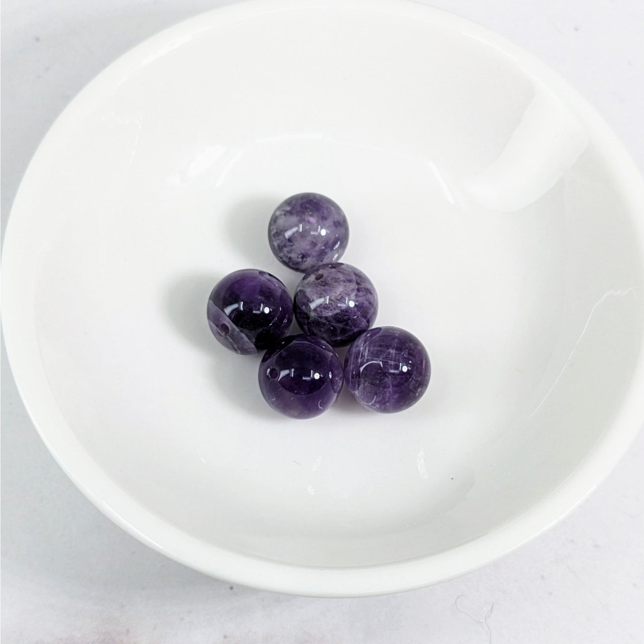 Banded Amethyst 10 mm Round Bead Pack #LV3620 displayed in a white bowl filled with purple marble