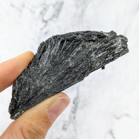 Thumbnail for A hand holding a piece of black coal from Black Kyanite 2 - 5’ Rough Stone #LV2425