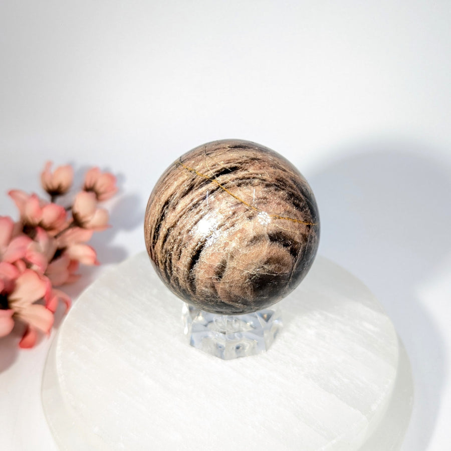 Polished black moonstone sphere with aventurine stripes on crystal stand