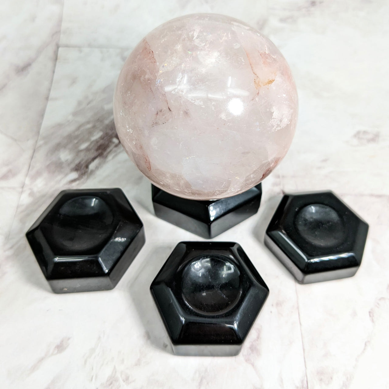 Pink quartz sphere with black hexagons on marble table in Black Obsidian Sphere Holder