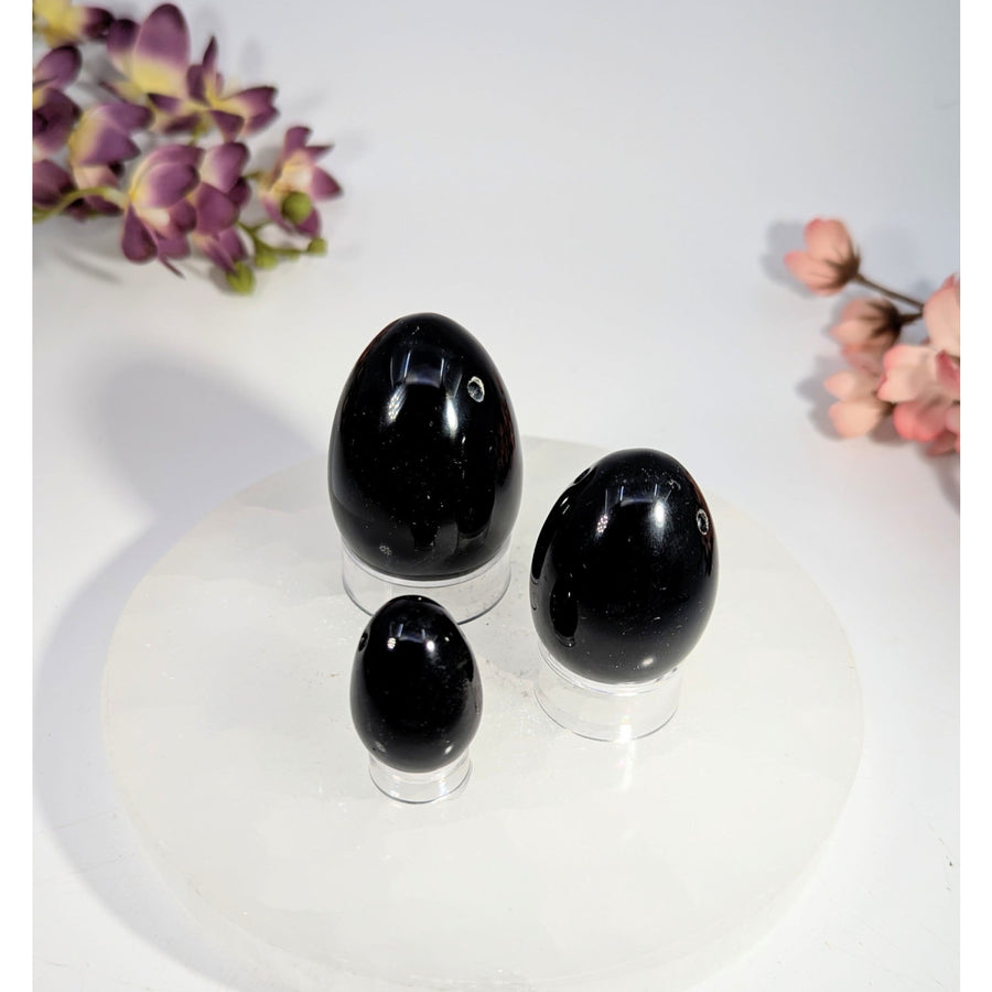 Three black obsidian yoni eggs with hole, 1-2 inches on acrylic stands