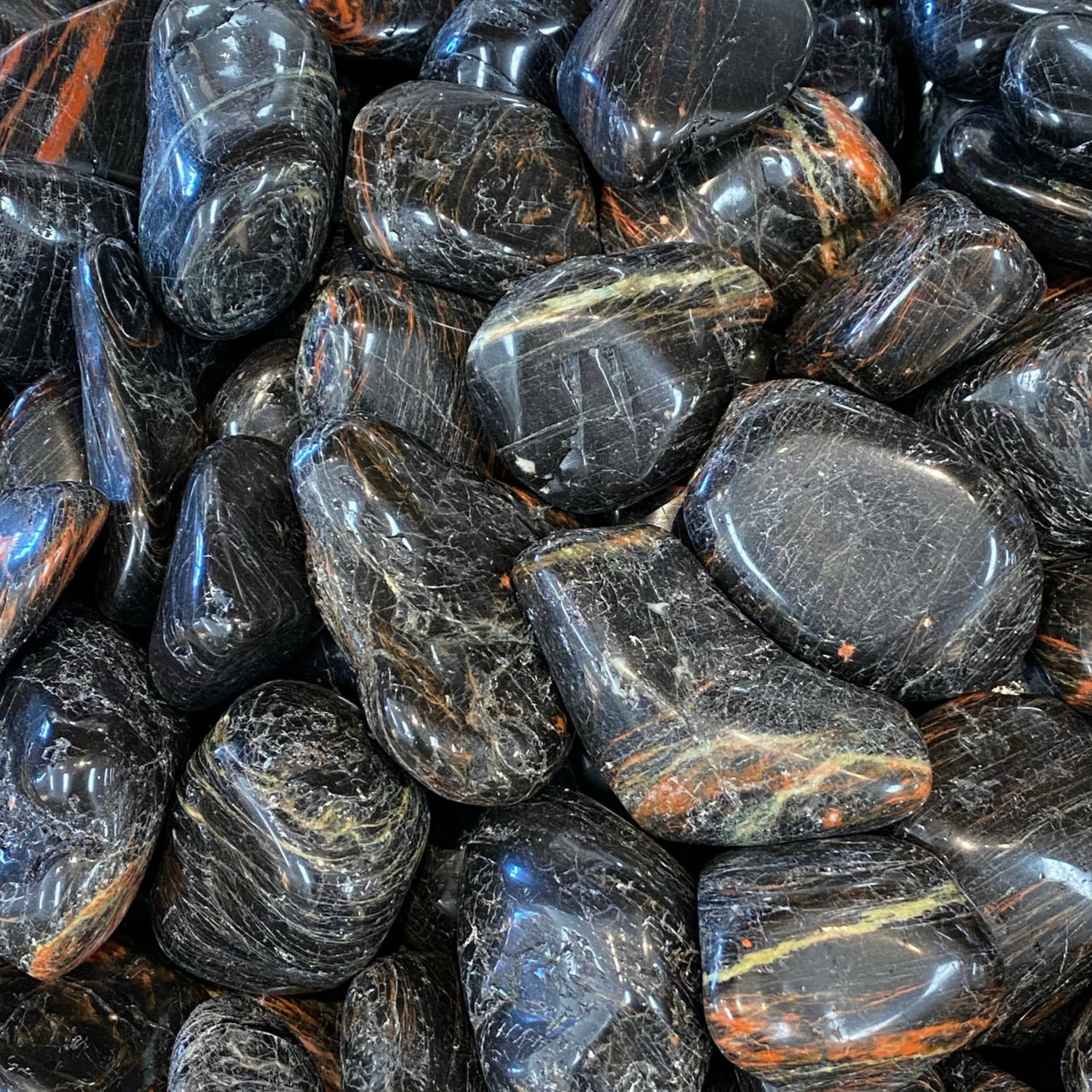 Polished black tourmaline pebbles with orange and blue streaks for decor and healing