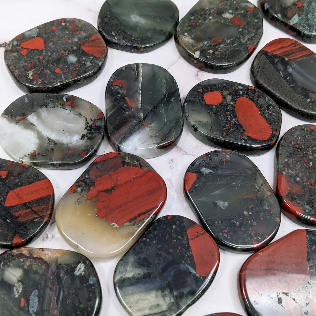 Close-up of various colored rocks on a table showcasing Bloodstone 1.7’ Flat Palmstone #SK9731