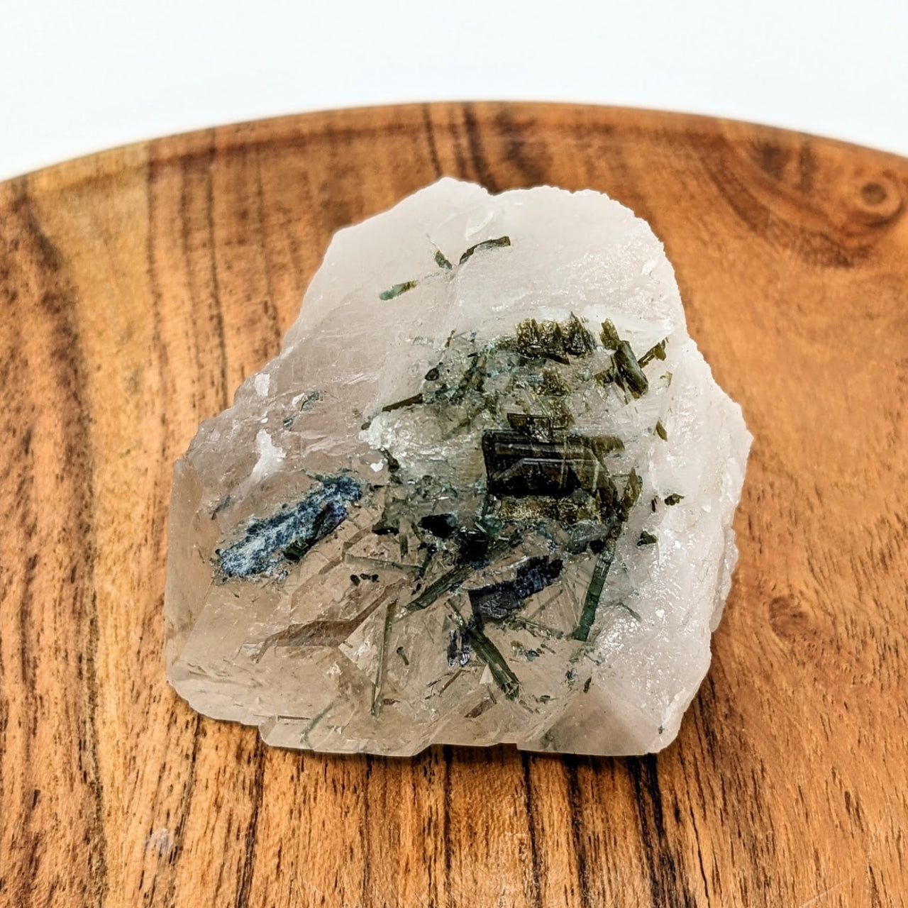 A piece of white quartz on a wooden board with a smoky quartz rough point