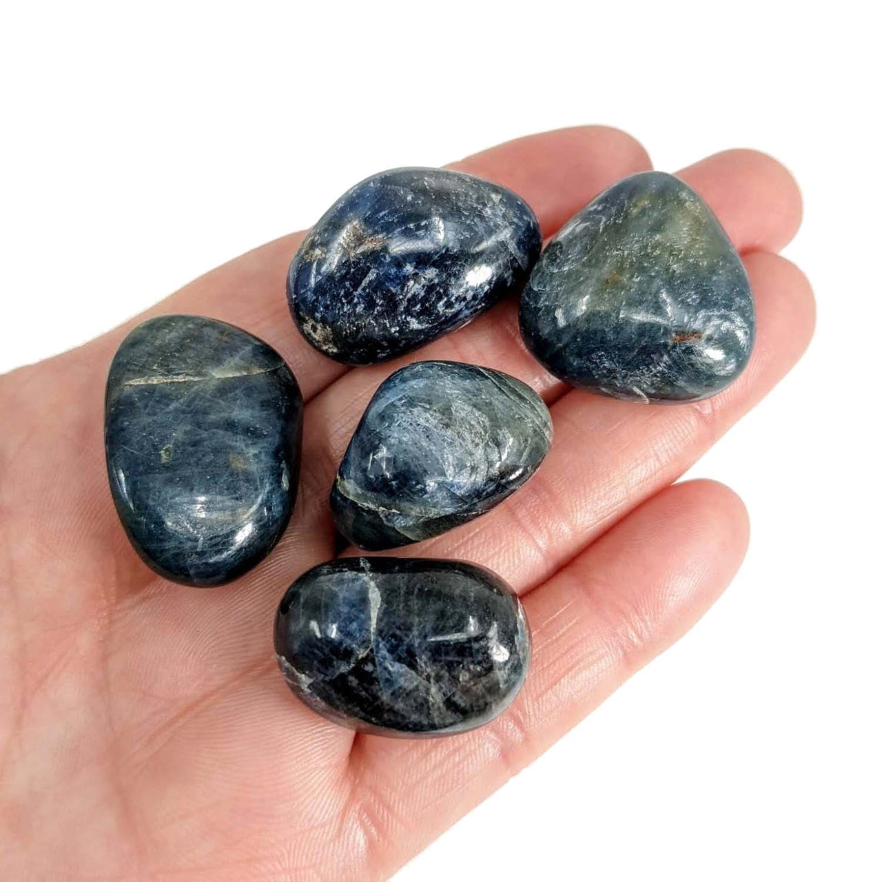 A hand holding five Blue Sapphire Tumbled Stones, showcasing their unique colors