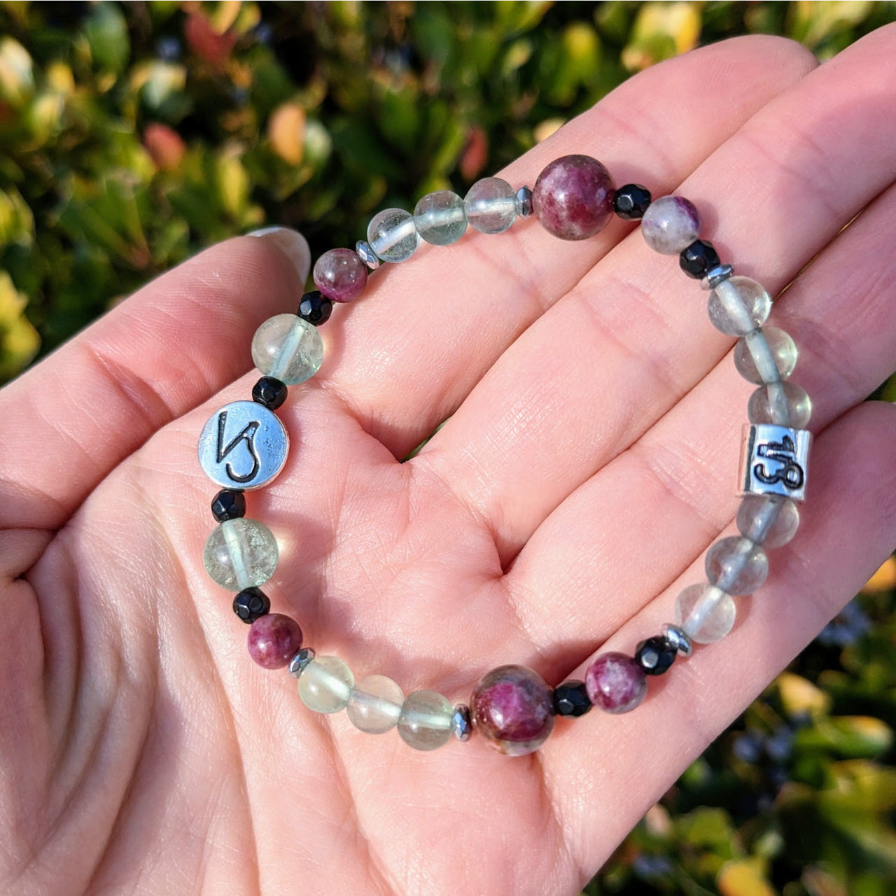 Hand holding a Capricorn Zodiac Handmade Beaded Bracelet with faceted beads and a silver charm