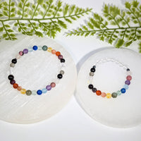 Two colorful handcrafted chakra rainbow crystal bead bracelets with gemstones displayed on white selenite plates