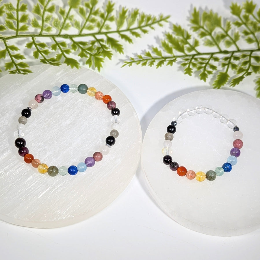 Two colorful handcrafted chakra rainbow crystal bead bracelets with gemstones displayed on white selenite plates