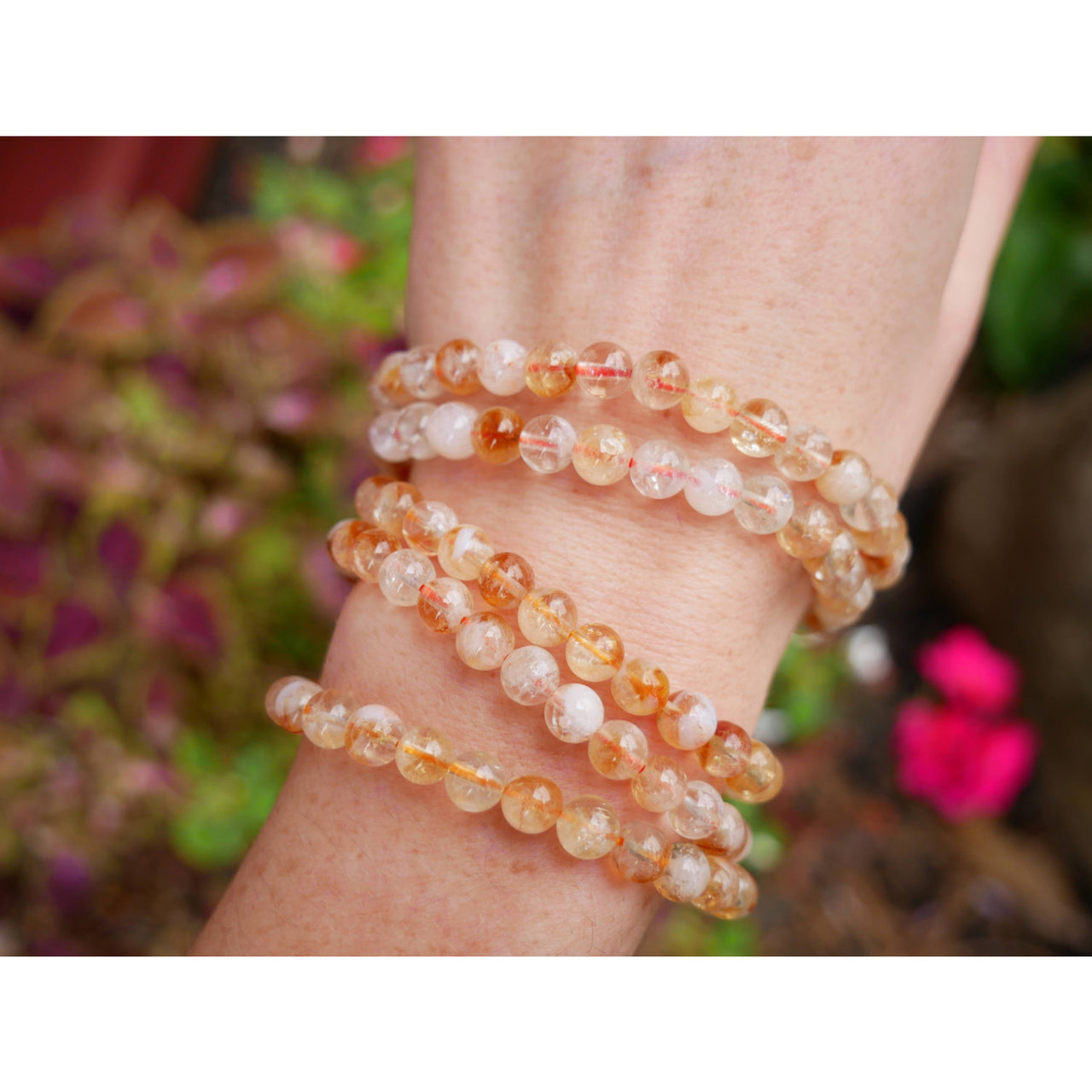 A delicate stack of four translucent orange and white citrine 6mm beaded bracelets worn on a wrist