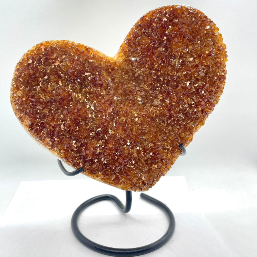 Sparkly orange heart-shaped Citrine crystal on black metal stand displayed in product EQ #H066