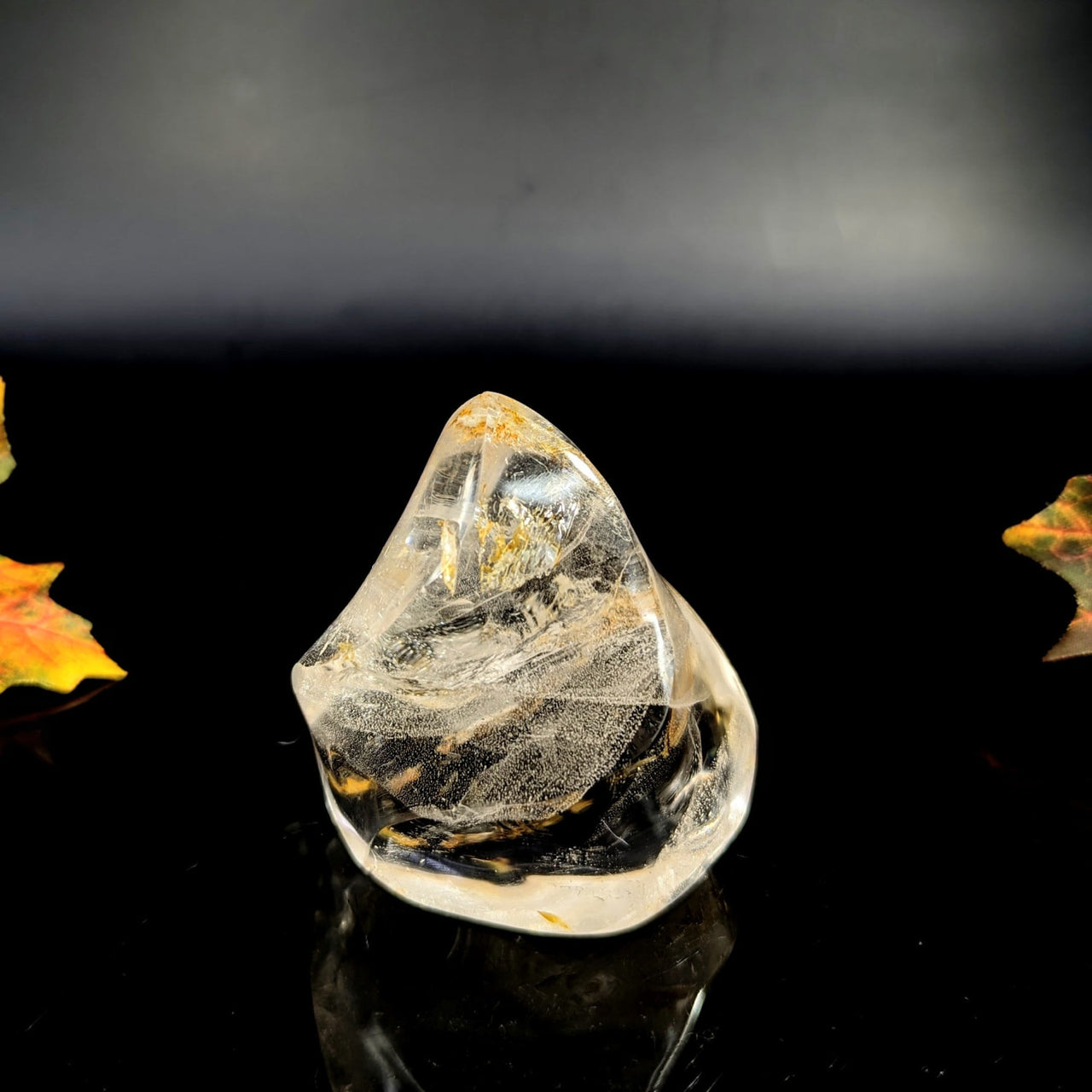 Golden quartz crystal point with black veining on reflective surface