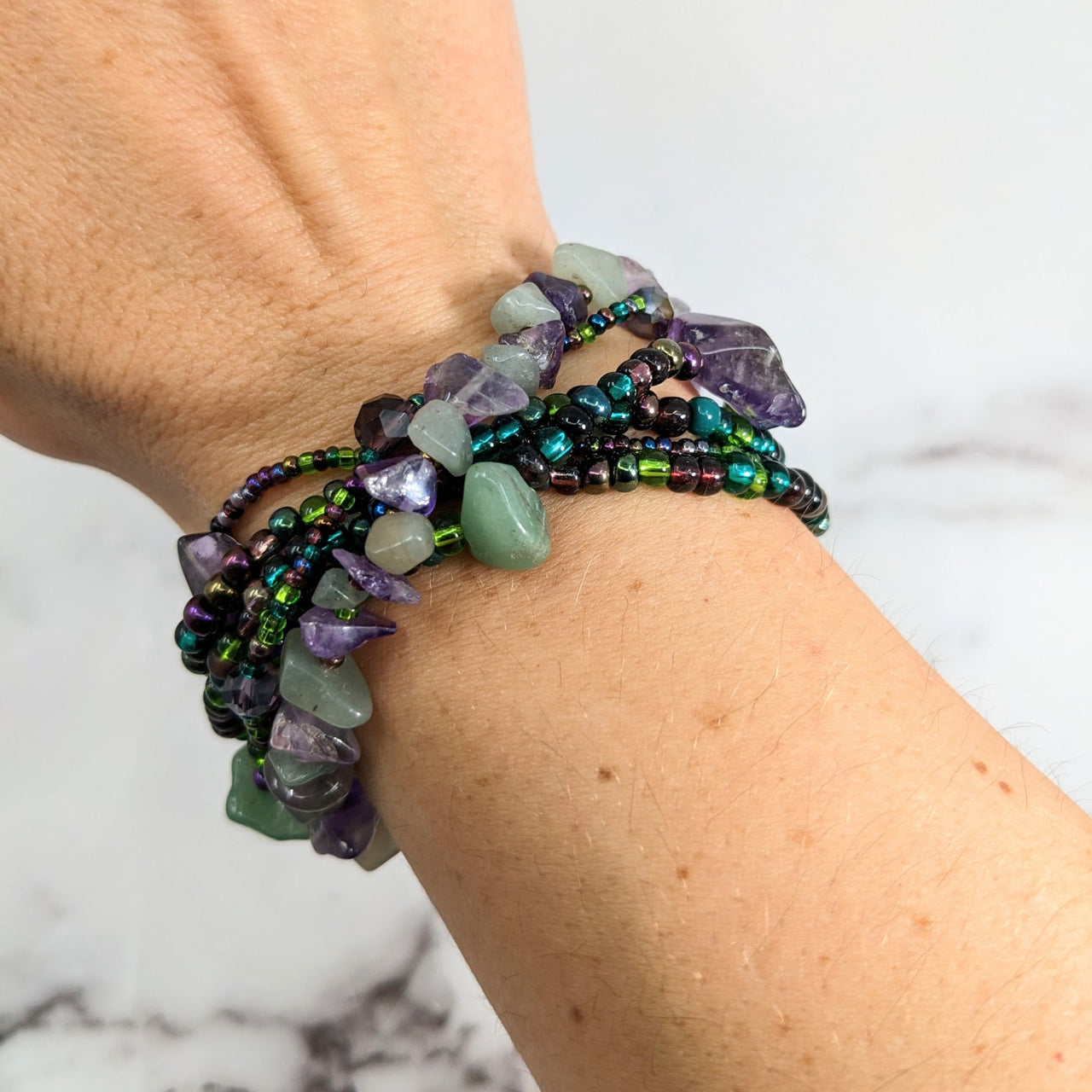 A woman’s hand wearing Crystal Beaded Bracelet with green aventurine and purple beads