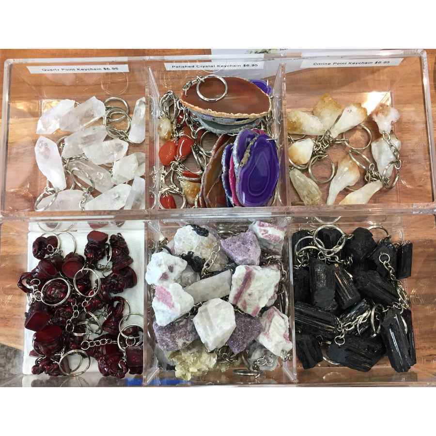 Clear acrylic display boxes hold assorted crystal keychains including quartz, purple agate, black tourmaline, and red resin charms