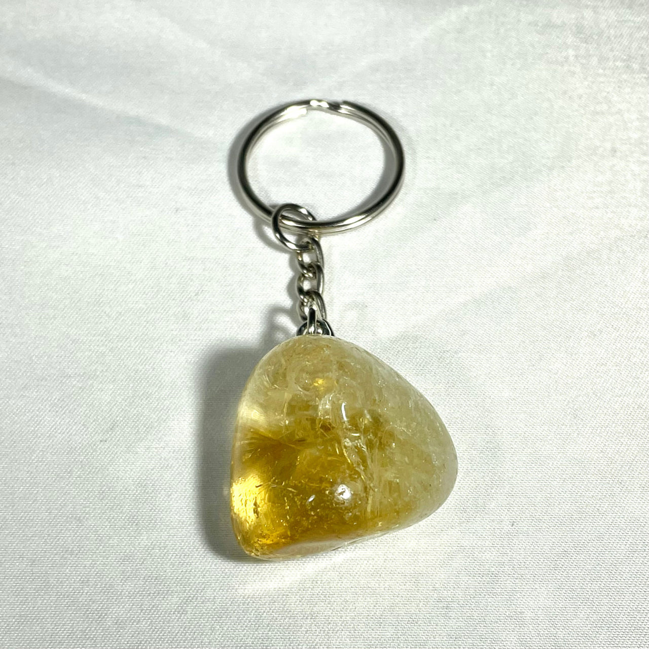 A translucent yellow citrine crystal keychain with smooth triangular shape and silver metal ring and chain from crystal keychain assorted Q106