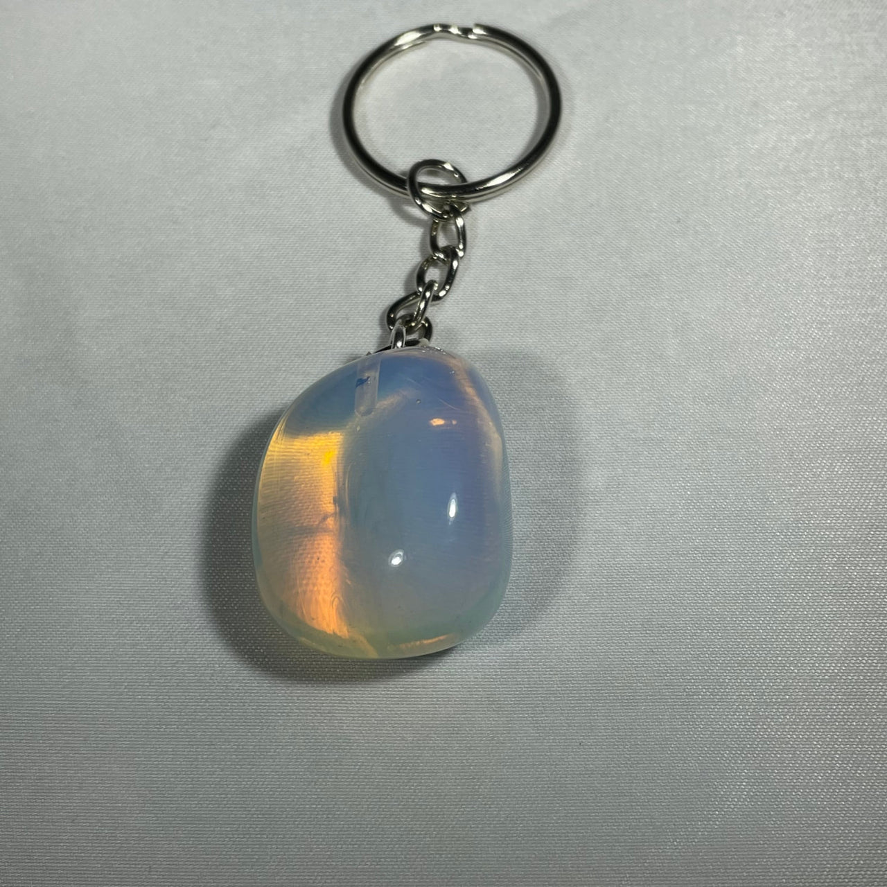 A smooth teardrop-shaped opal crystal keychain with a silver-toned metal ring and chain for everyday use
