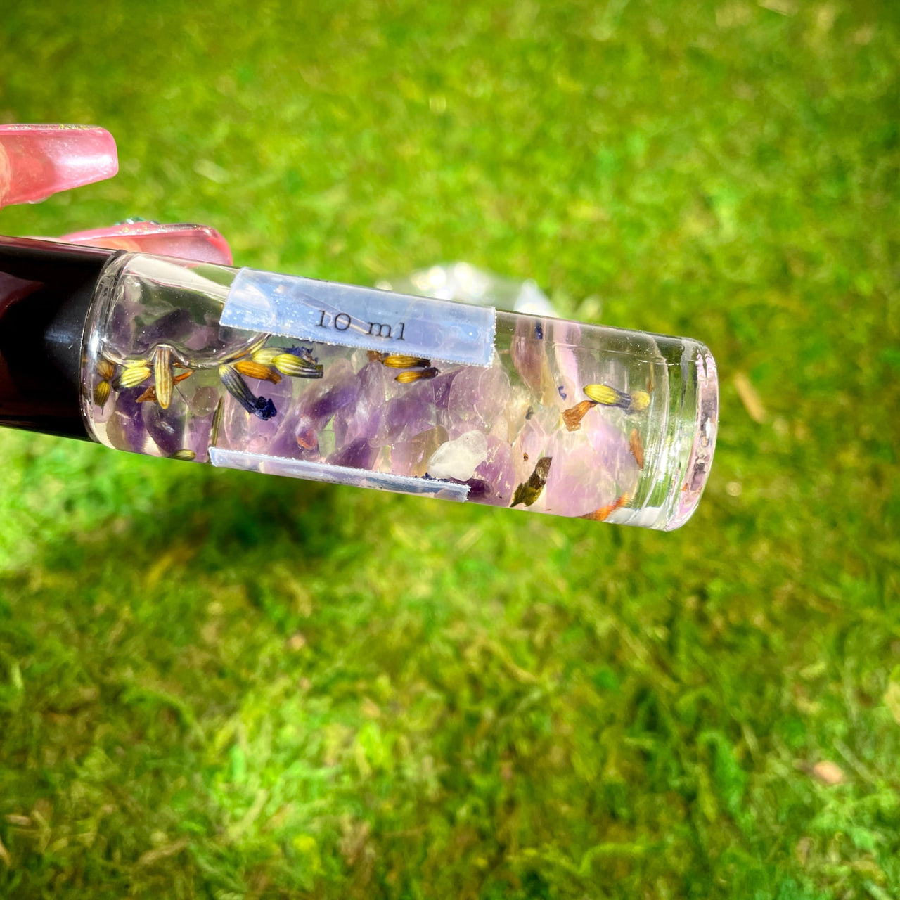 A person holding a floral-filled glass bottle of Crystal Perfume 10ml Roller #Q217