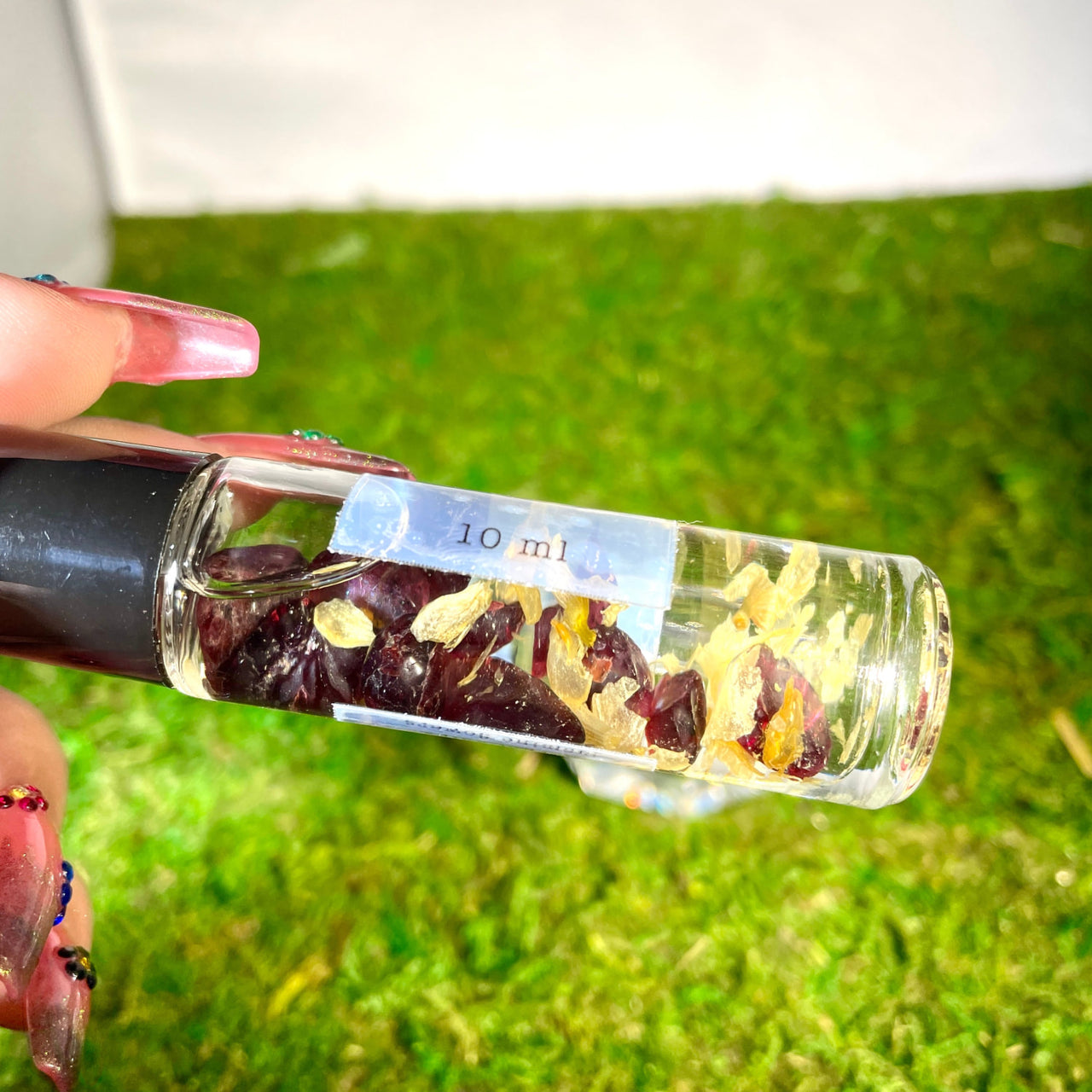 Hands holding a Crystal Perfume 10ml Roller #Q217 with dried fruit and nuts inside