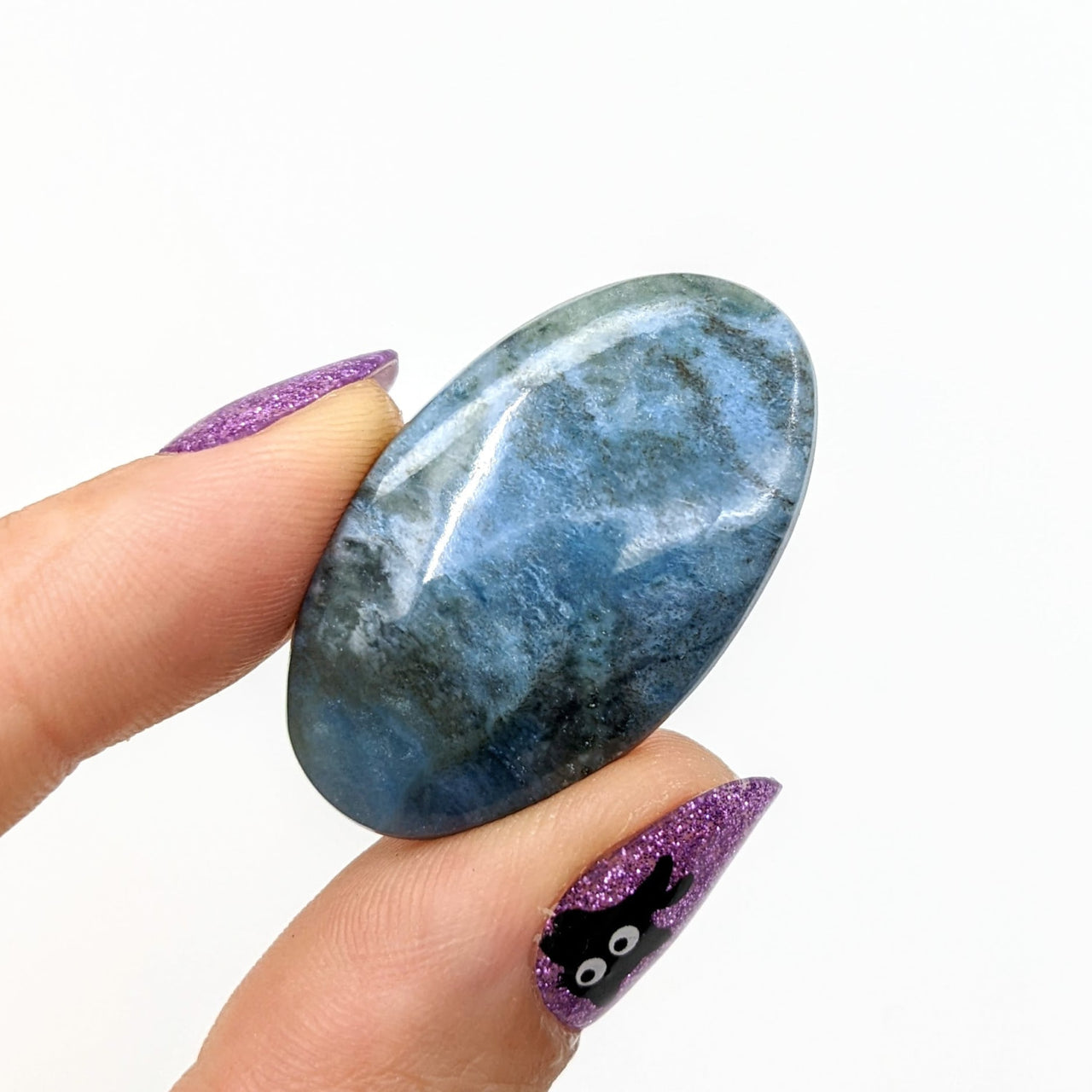 Person holding Dianite Grade AA 1.4’ blue stone with purple glitter (#LV1237 Cabochon)