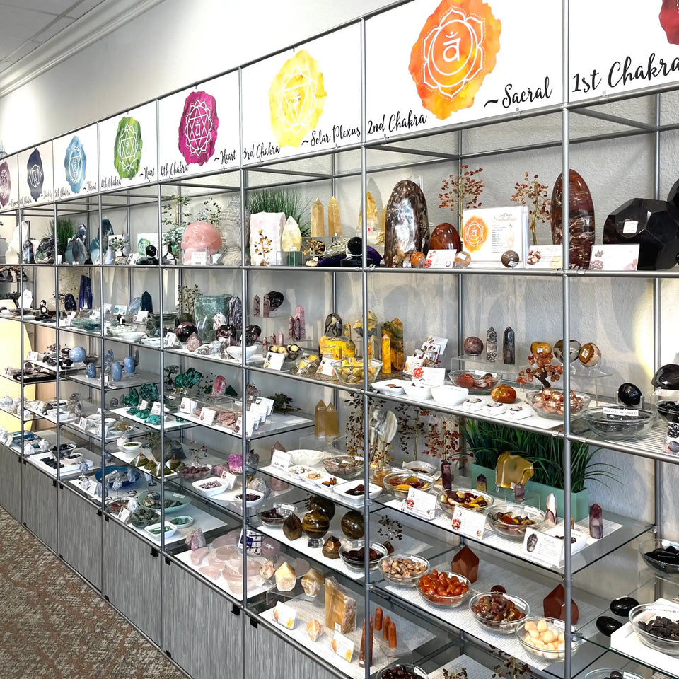 Display case filled with crystals, gemstones, and chakra-themed spiritual items arranged on multiple glass shelves.
