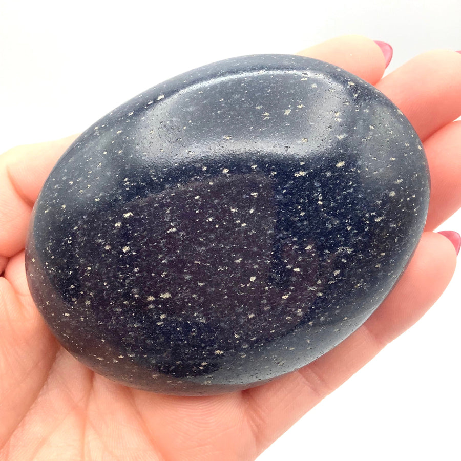 A hand holding a Dumortierite Pebble (204g) #SK3508 with black stone and white specs