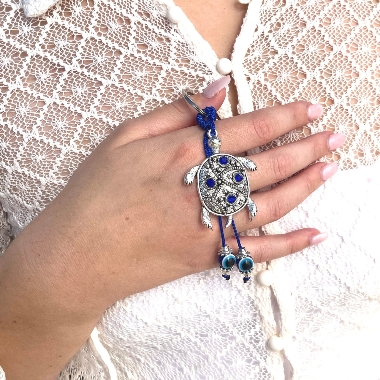 A woman wearing an evil eye bracelet with a blue bead and a silver turtle