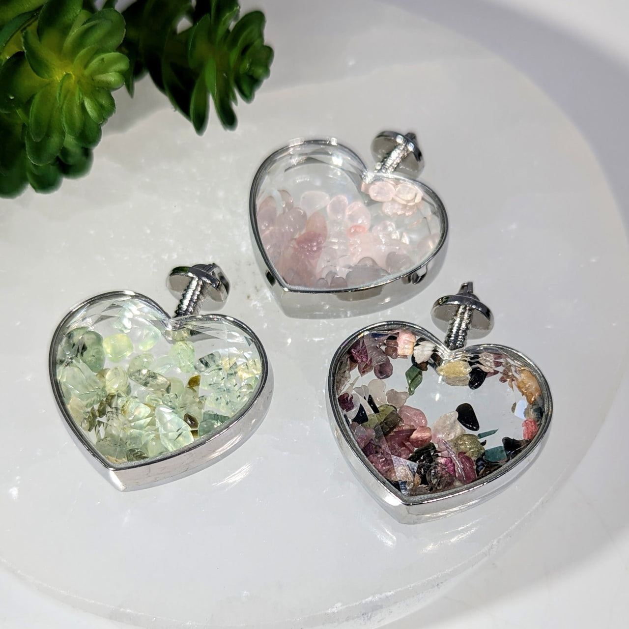 Three heart-shaped crystal pendant charms with silver frames and colorful gems