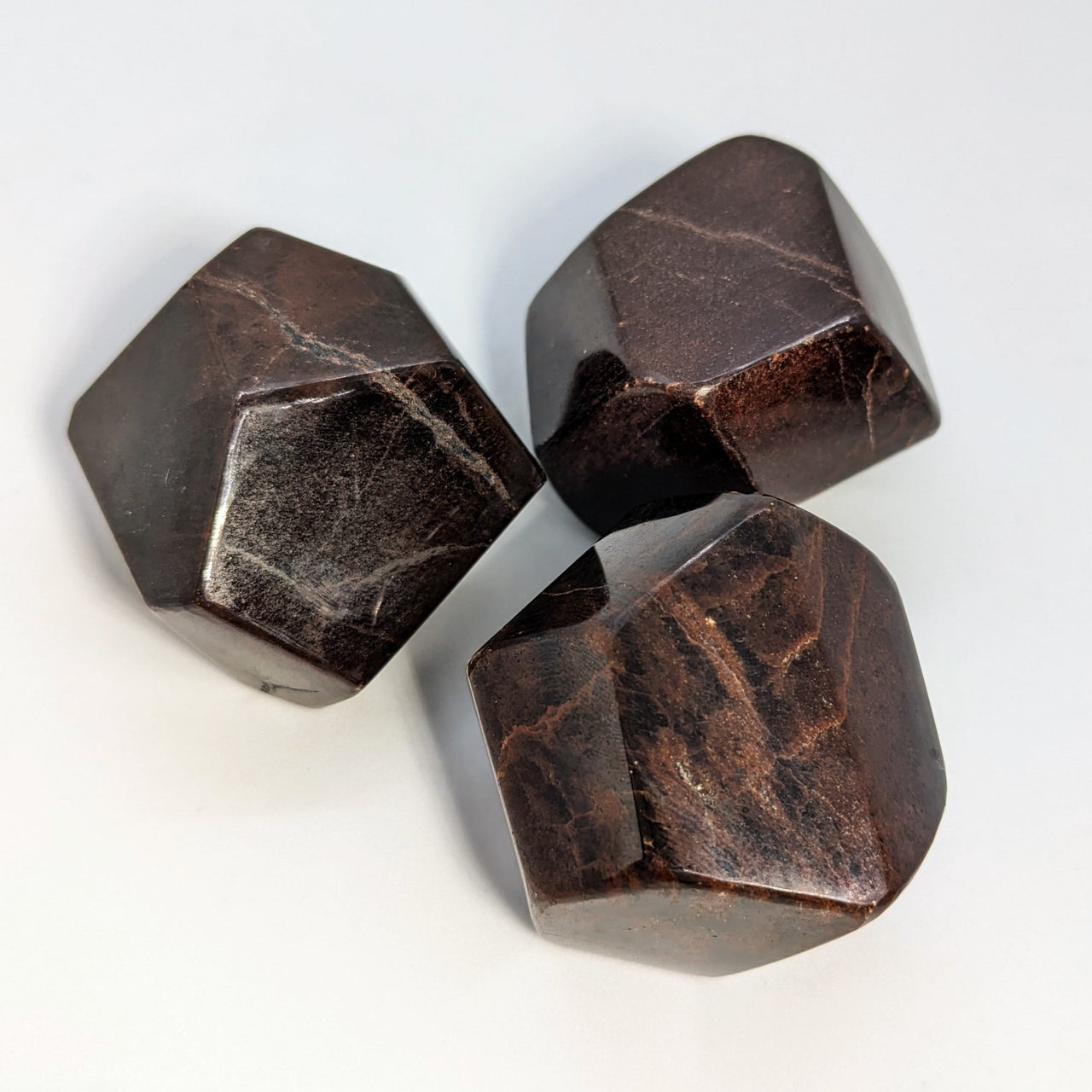 Faceted Red Garnet Polygon Polished Stone #SK8089 with three brown marble dices on white background