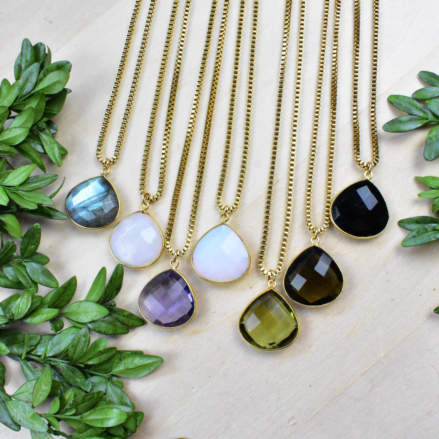 Elegant gold teardrop pendant necklaces with faceted gemstones in blue, lavender, white, black, green