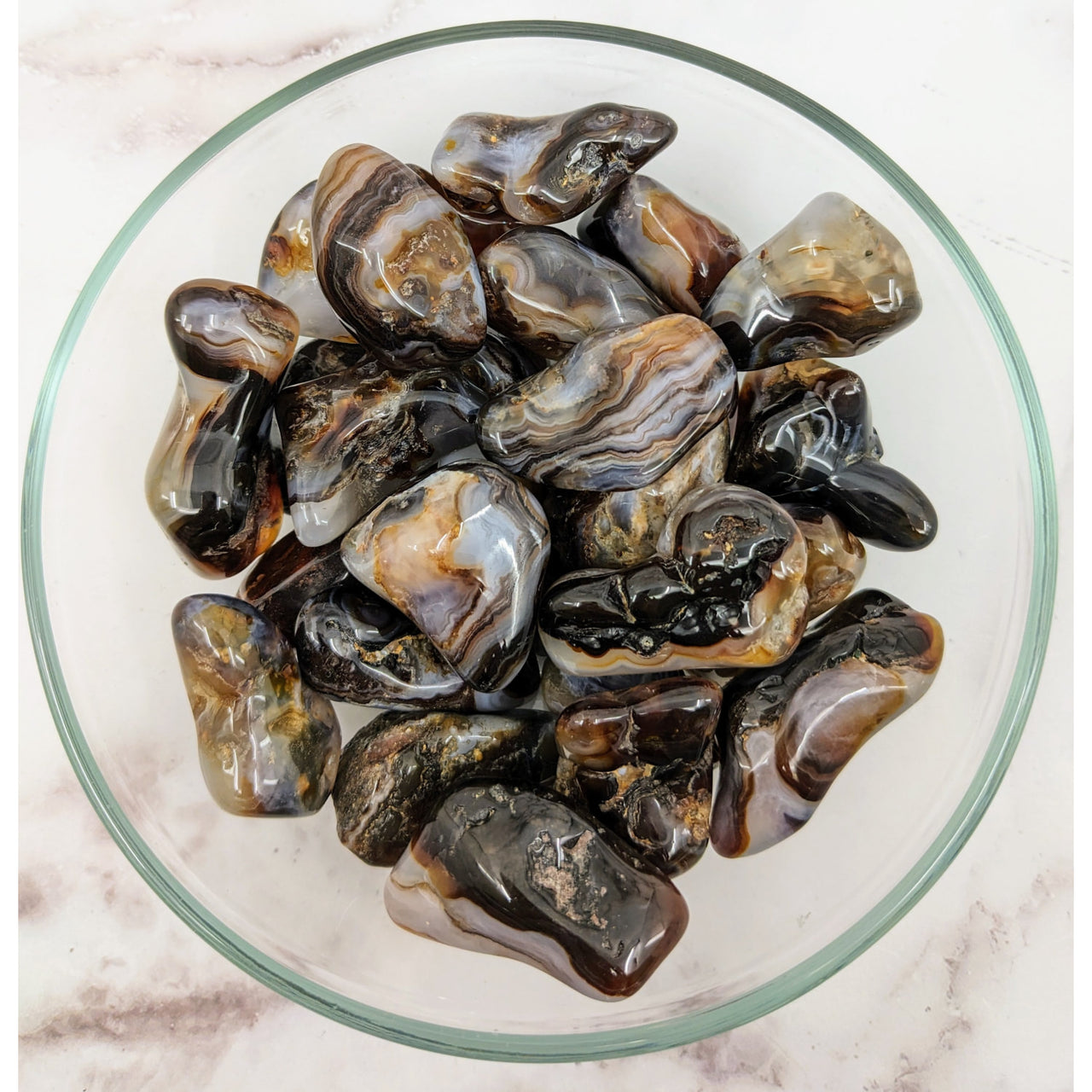 A bowl of musselins alongside ’Fire Agate 1.2 - 1.7’ Tumble Stone #LV3419’ tumbled stones