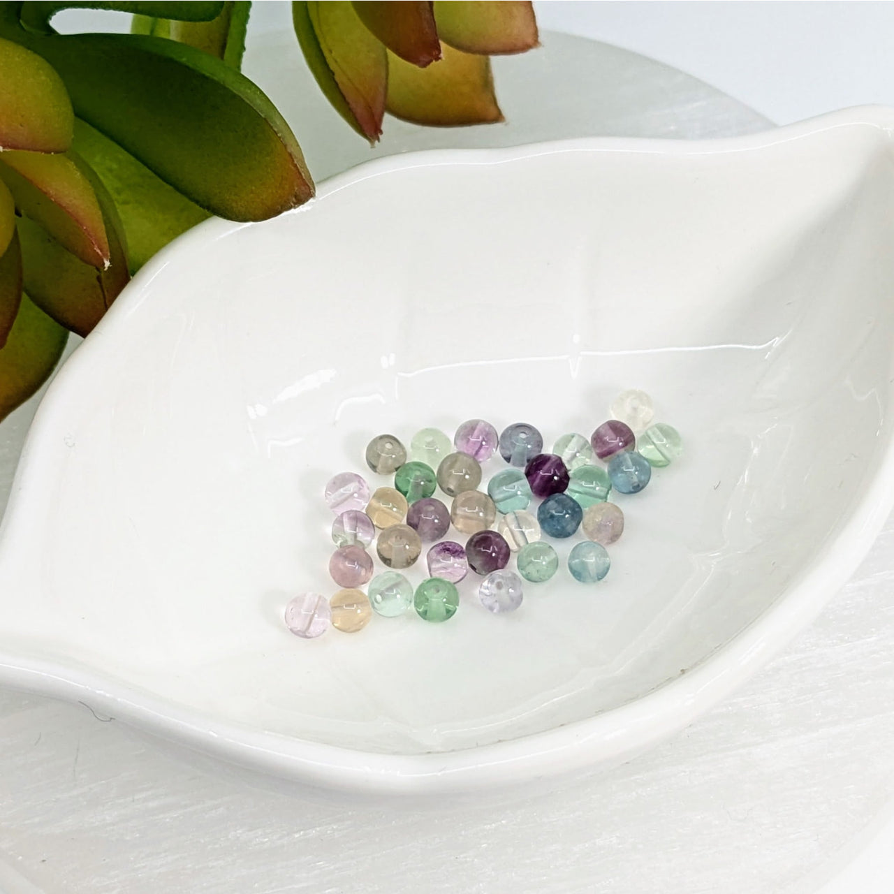 Colorful fluorite 4mm mini round beads in a white ceramic dish for crafting