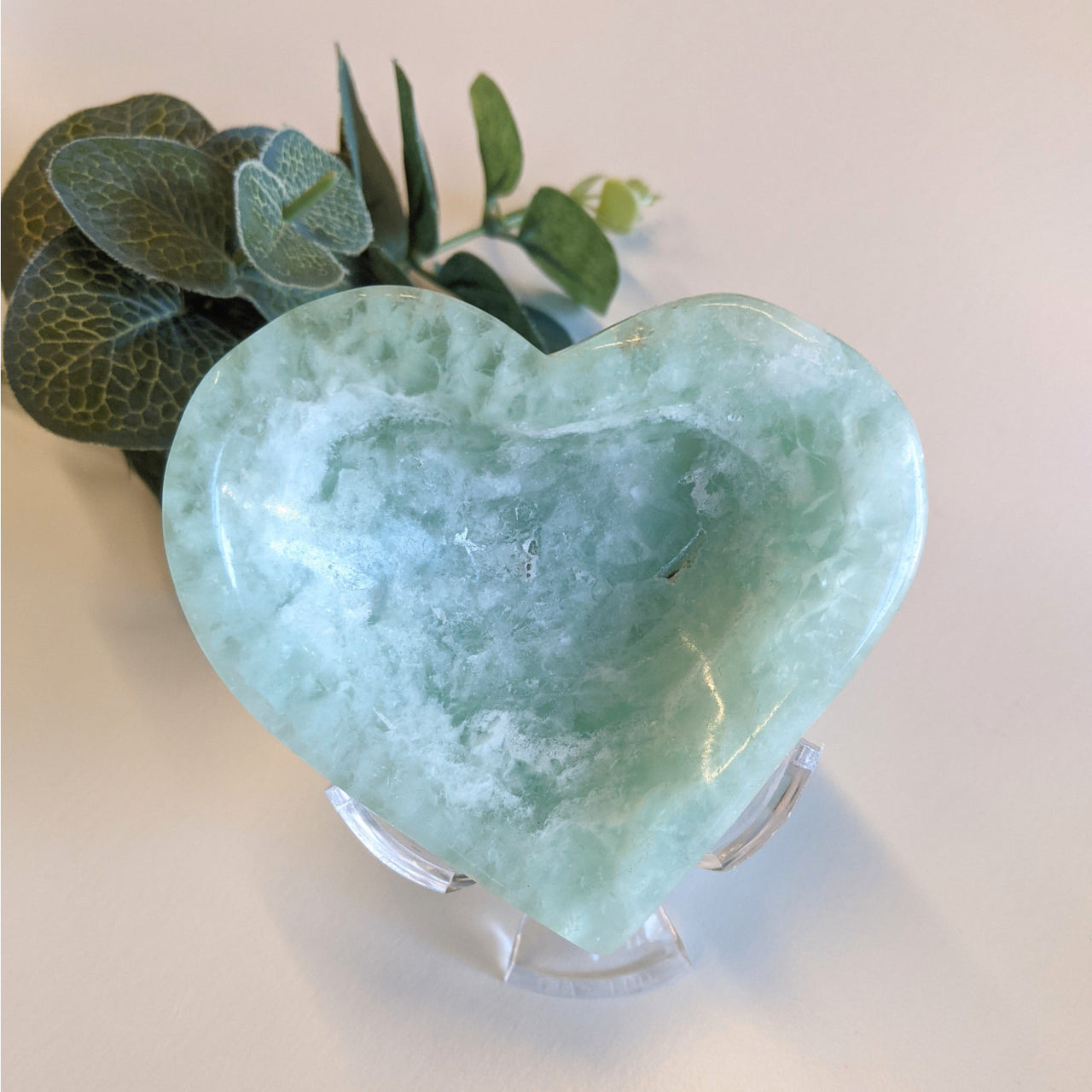 Fluorite heart bowl dish with stand, heart-shaped vase, and plant in background