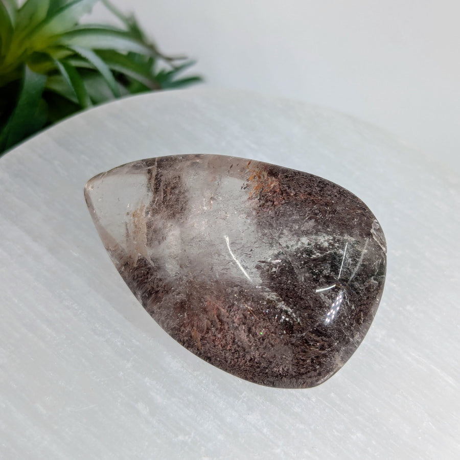 A 2.2 inch polished teardrop garden quartz crystal with translucent body and dark brown inclusions