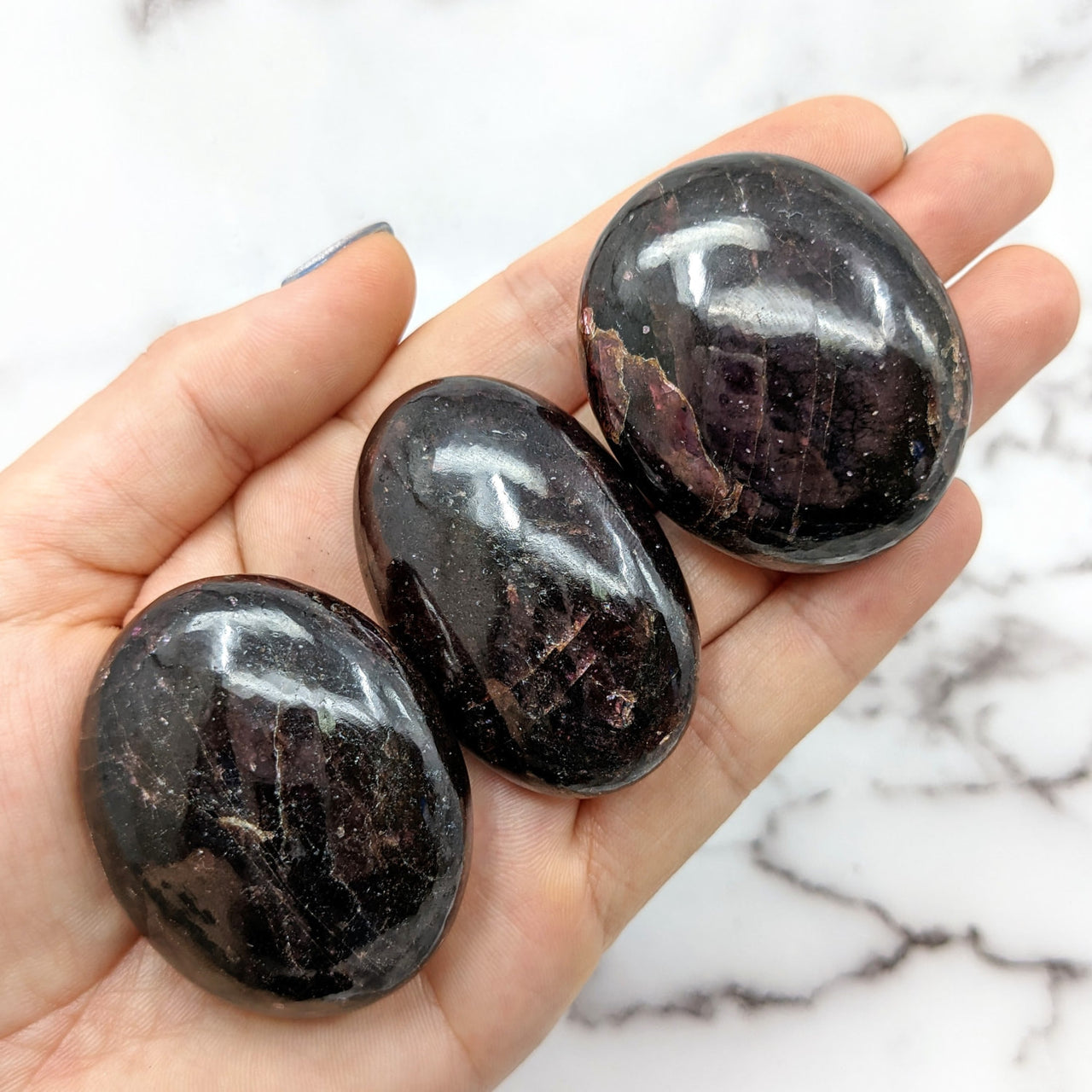 Three black Garnet palm stones on hand, displayed on a marble surface