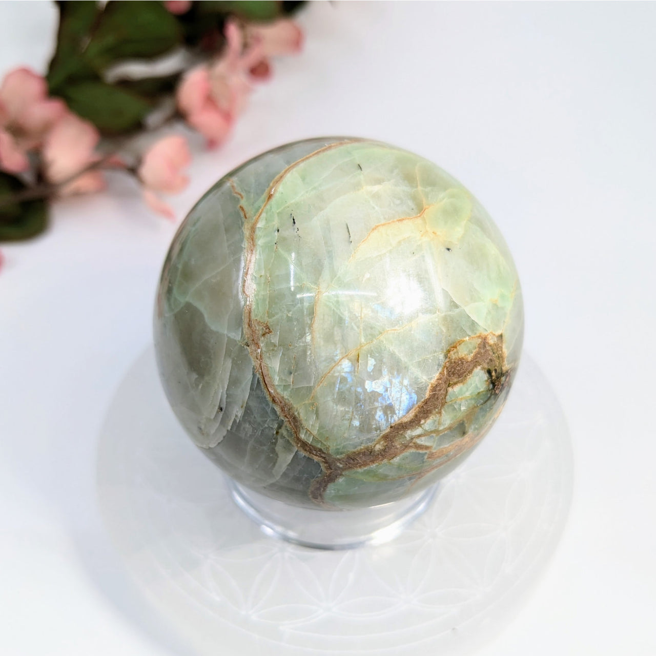 Polished green opal sphere with golden-brown veining on a clear stand for item tier benefits